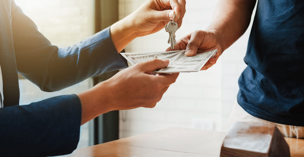 Main tenant un billet canadien à côté d'une fenêtre en PVC abîmée.